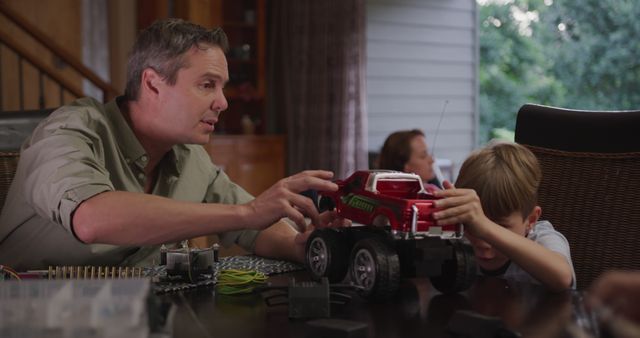 Happy caucasian father and son at table playing with toy car at home. Family, domestic life, fun and lifestyle, unaltered.