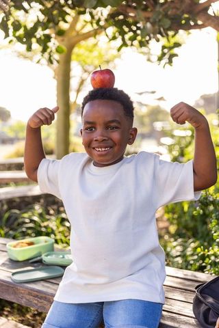 Playful african american boy balancing apple on head while flexing arms in park