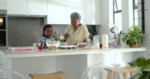 Grandmother and girl baking together on bright modern kitchen island, mixing batter
