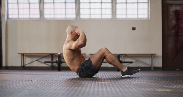 Muscular, shirtless caucasian man with shaved head doing sit ups. health and fitness training at gym.