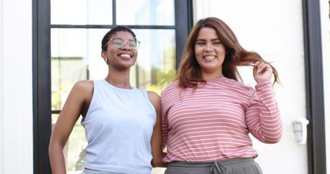 Smiling diverse female friends standing together by glass door sharing warm friendship