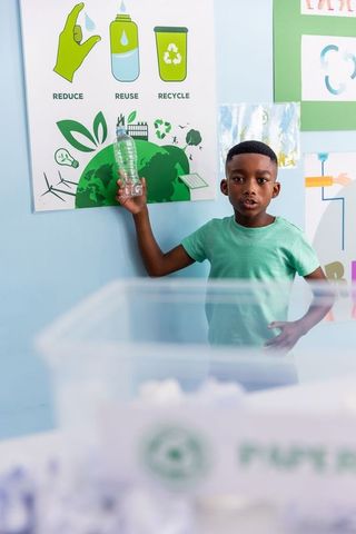 African american boy holding crushed plastic bottle teaching recycling at school poster