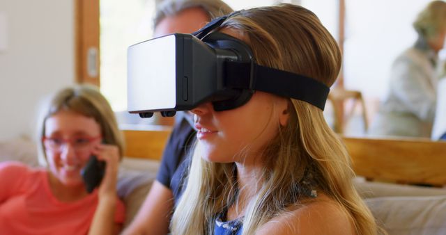 Teenage Caucasian girl explores virtual reality at home. She's immersed in technology while another girl observes with curiosity.