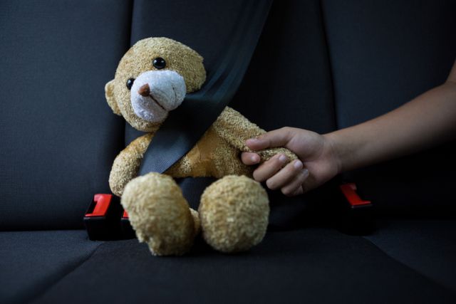 Close-up of teenage girl sitting with teddy bear in the back seat of car