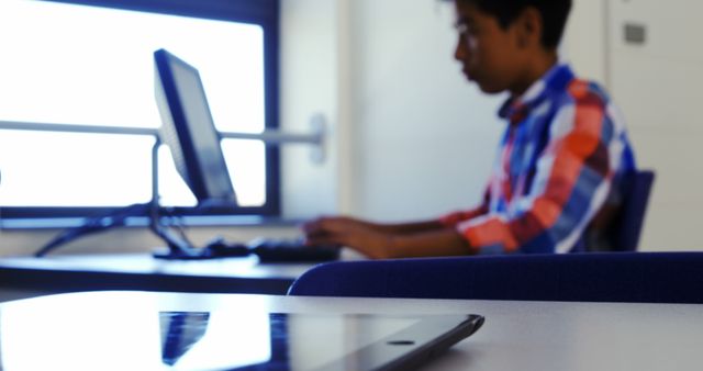 Student focusing on computer during classroom session. This can be used to illustrate modern education, digital learning environments, and the integration of technology in schools.