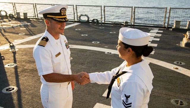 Navy officer and sailor shaking hands on flight deck in white uniforms at sunset