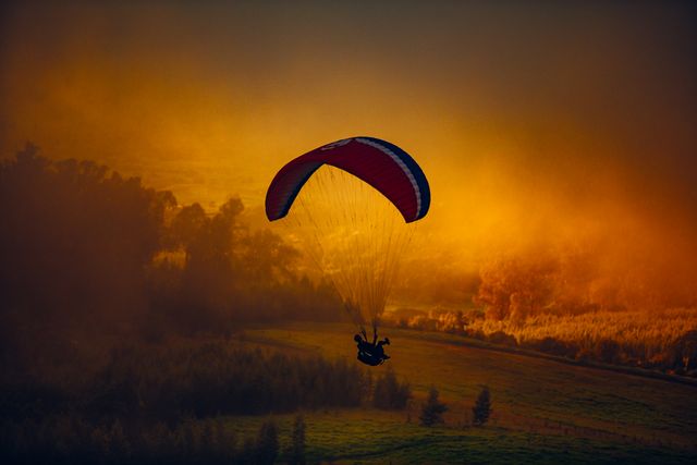 Paraglider soaring gracefully over landscapes during golden sunset, showcasing thrill of paragliding. Perfect for travel blogs, adventure magazines, outdoor activity promotions, or websites about extreme sports and nature exploration.
