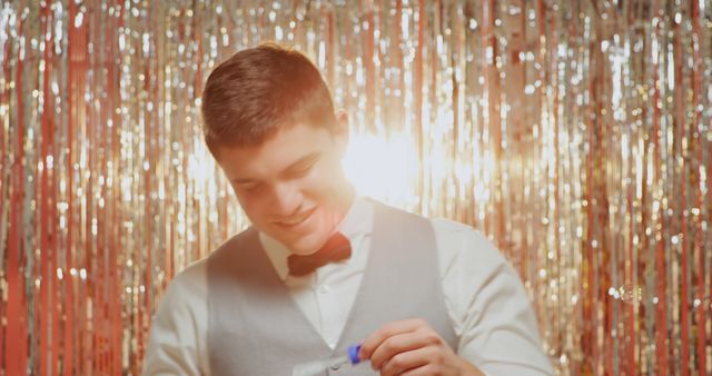 Young Caucasian man adjusts his bow tie at a festive event. Dressed in formal attire, he's preparing for a celebration or special occasion indoors.
