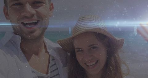 Couple smiling and taking selfie on beach with straw hat and sun flare