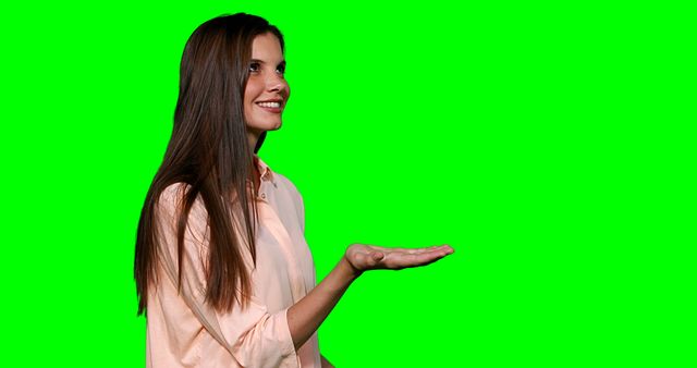 Young woman with long hair smiling and holding open hand on a green screen background. Perfect for promoting products, advertising, presentations, or any project requiring an isolated figure with a customizable backdrop. Useful for designers needing blank space for inserting text or images.