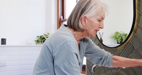 Senior Woman Using Bathroom Sink with Elegant Minimalist Decor