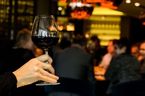 Hand Raising Red Wine Glass Toasting at Busy Restaurant Bar Celebrating Night Out