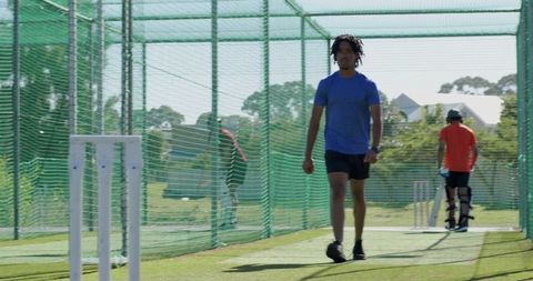 Male athlete walking through cricket nets with stumps on sunlit turf, training moment