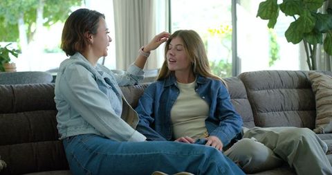 Two friends relaxing on sofa sharing conversation and gentle hair touch in cozy living room