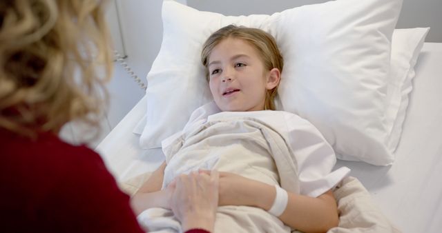 A child lying comfortably in a hospital bed with a soft smile while a visitor holds their hand. This scene illustrates care and support during recovery. It can be used in health care magazines, medical brochures, hospital websites, or campaigns focused on patient care and family support.