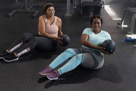 Two african american women doing seated russian twist with medicine ball in gym