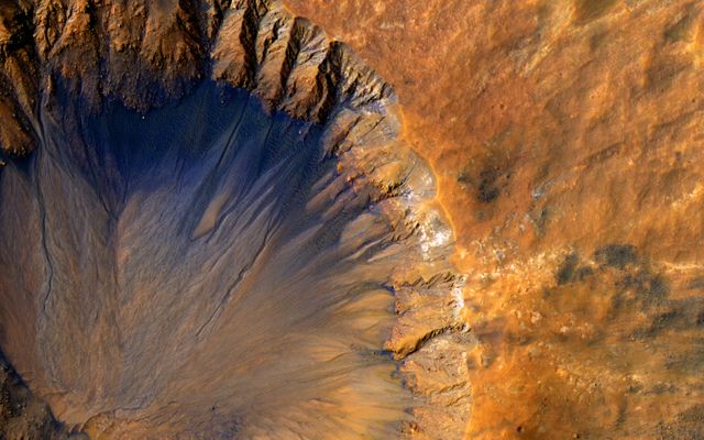 Vivid image shows detailed view of an impact crater on the surface of Mars, showcasing erosion patterns and terrain color variations. Ideal for use in educational materials, space exploration articles, astronomical studies, and as a visually engaging background.