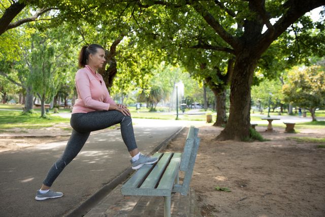 Senior Caucasian woman working out in the park wearing sports clothes, stretching her legs on a bench. Retirement healthy lifestyle activity.