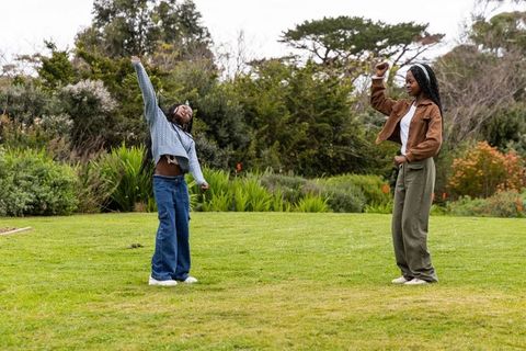 African american teen friends dancing and mirroring moves on park lawn streetwear style