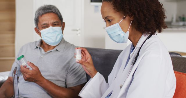 Healthcare professional provides in-home medical consultation to senior patient during pandemic. Both wearing face masks. Image can be used in articles or brochures on home care services, elderly healthcare, pandemic safety measures, and nursing practices.