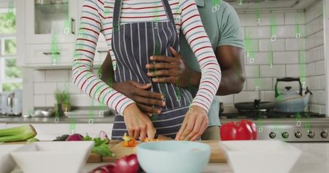 Couple embracing while chopping fresh vegetables on modern white kitchen counter