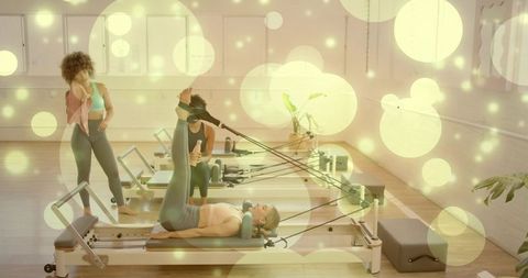 Reformer pilates class with instructor guiding leg stretches in bright wellness studio group trainin