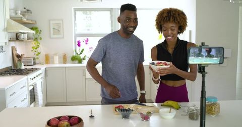 African american couple filming healthy breakfast bowl in bright modern kitchen