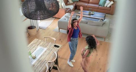 Diverse friends dancing joyfully in bright open-plan living room with rustic dining table