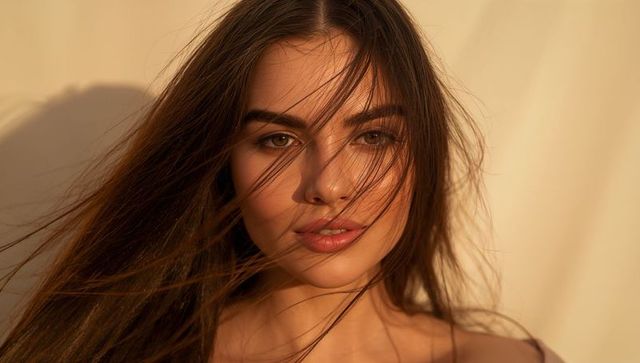 Sunlit studio portrait of female model with flowing hair and warm beige glow for beauty