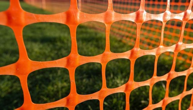 Orange safety fence stretching across grassy field showing grid texture and sun glare