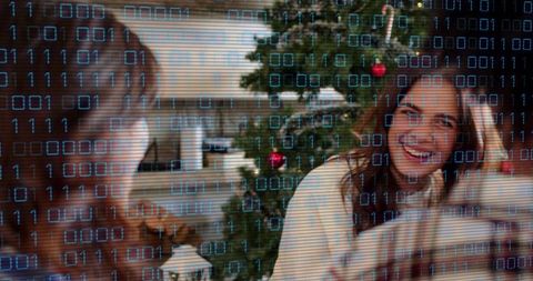 Smiling woman leaning by Christmas tree with digital binary overlay holiday technology