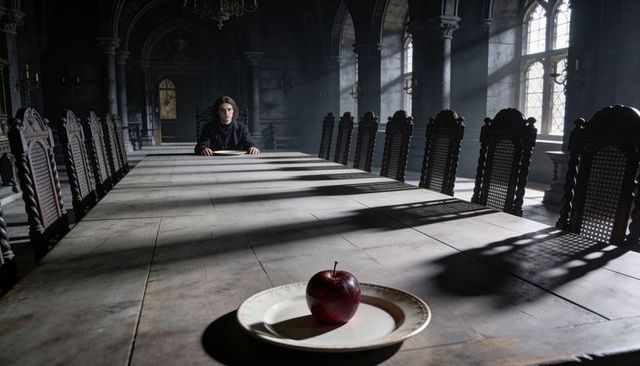 Solitary man seated at long gothic table with red apple on plate, dramatic sunlight