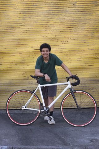 African american man leaning on white fixed-gear bike in front of weathered yellow metal door