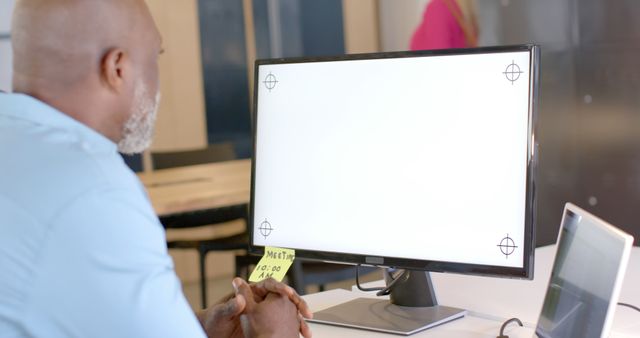 Mature man working on a computer with screen showing calibration marks. Useful for themes around office work, design, technology, and professional environments.