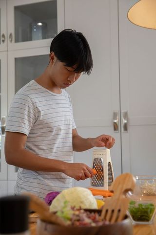 Man preparing fresh meal by shredding carrots in rustic kitchen