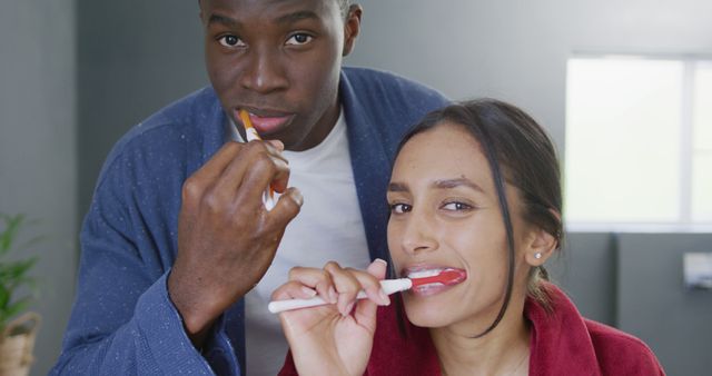 Image of happy diverse couple brushing teeth and smiling in bathroom at home. Happiness, love, domestic life, and inclusivity concept.