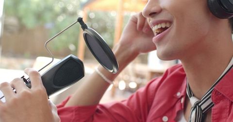 Asian Podcaster Recording Outdoors Adjusting Headphones by Garden Table