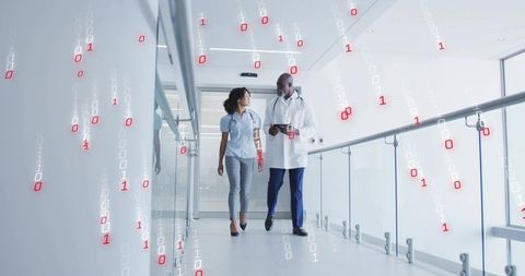 Medical professionals walking corridor using digital tablet with floating binary visuals