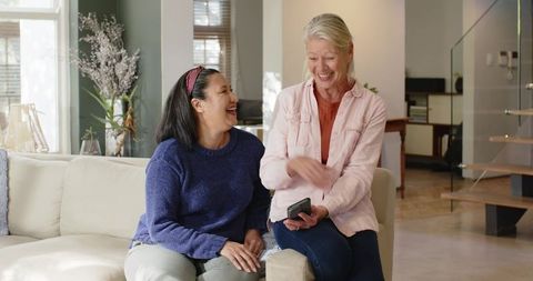 Senior Female Friends Laughing in Modern Living Room with Smartphone