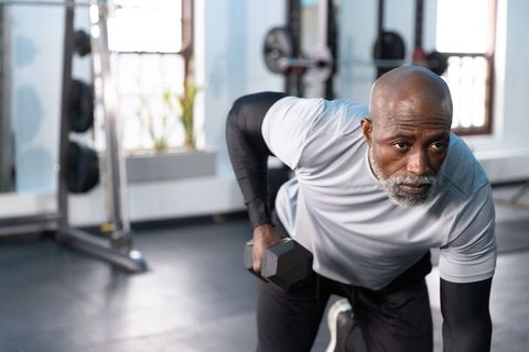 Senior african american man performing single-arm dumbbell row in sunlit gym