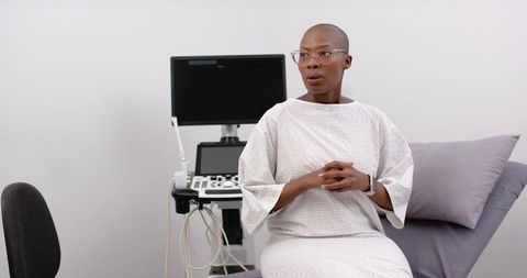 Waiting patient sitting on exam table in clinic gown beside ultrasound monitor
