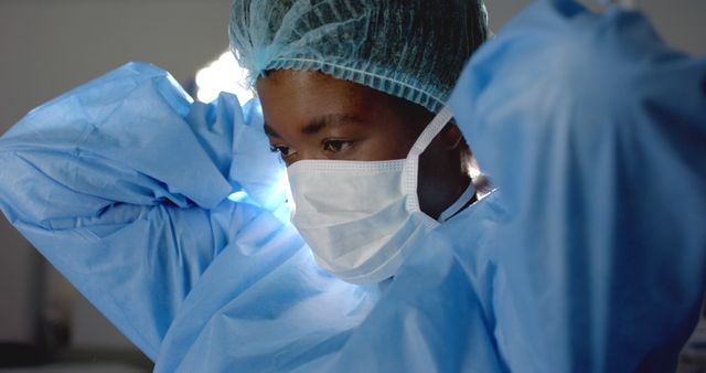African american female surgeon wearing face mask and medical gloves in operating room. Medicine, healthcare, surgery and hospital, unaltered.