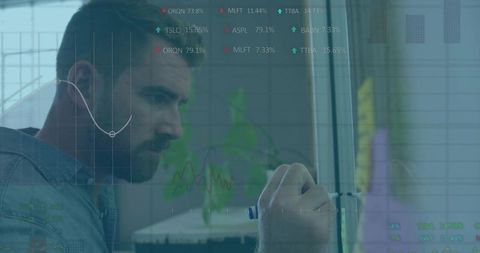 Senior male analyst writing on glass board with financial charts overlay analyzing data trends
