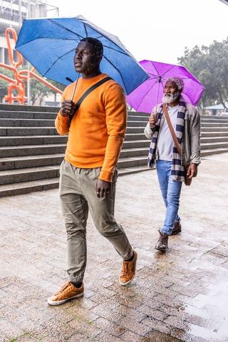 African american men walking in rainy urban plaza holding blue and purple umbrellas