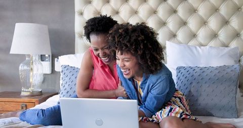 Mother and Daughter Laughing Together Using Laptop in Bedroom