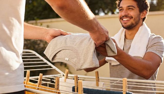 Smiling man handing folded t-shirt over drying rack on sunny backyard patio