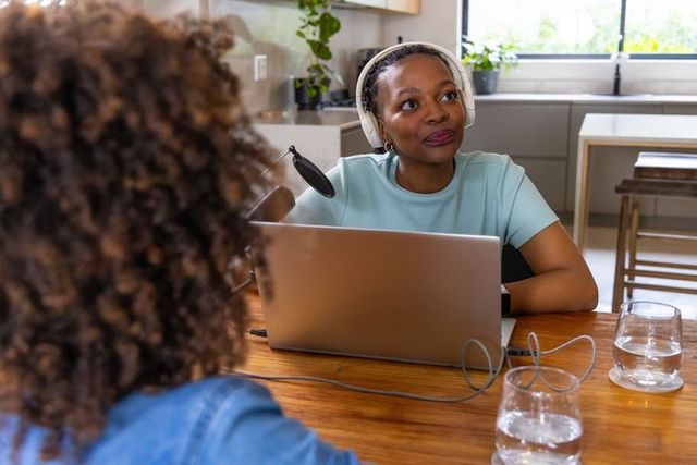 Recording podcast host interviewing guest in cozy bright home kitchen with laptop mic