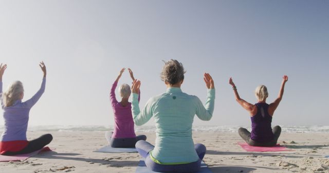 Group of senior women practicing yoga on beach with ocean in background. Ideal for promoting senior fitness, healthy lifestyle, physical activity, wellness programs, and ads focused on well-being and outdoor exercises.