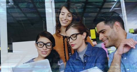 Diverse team collaborating over laptop in glass-walled coworking space with sticky notes