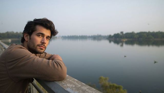 Contemplative young man leaning on bridge railing overlooking calm river in serene dawn